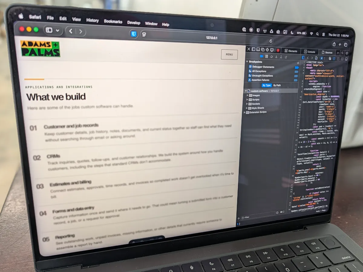 Angled view of a laptop showing an Adams + Palms website beside web development code.